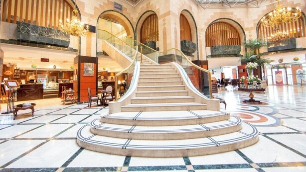 A grand lobby with a central staircase, marble flooring, and arched windows. - Dallah Taibah Hotel (Madinah)