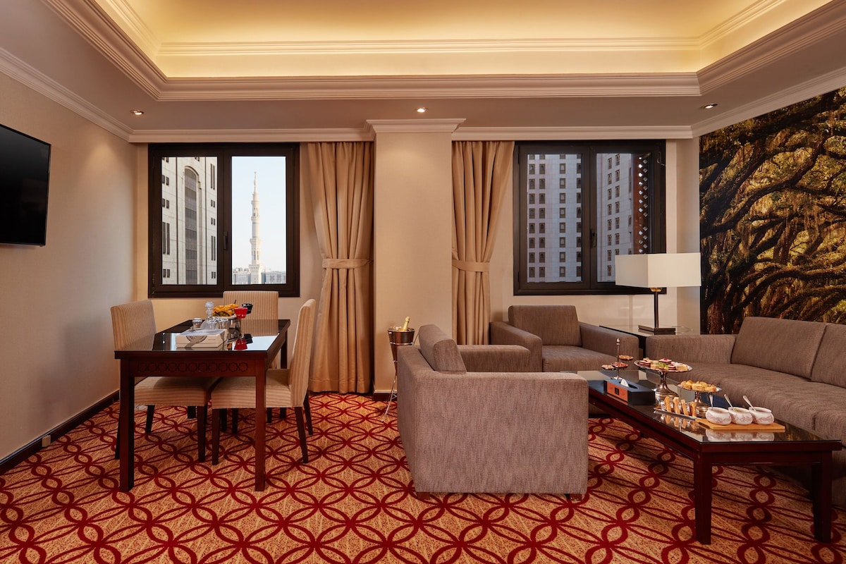 A hotel room with a dining table, two sofas, a coffee table, and a large window with curtains.