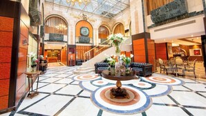 A hotel lobby with a grand chandelier, a central floral arrangement, a clock, and a staircase. - Dallah Taibah Hotel (Madinah)