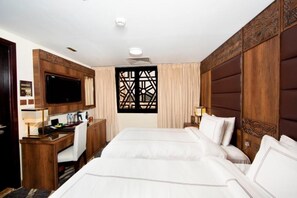 A hotel room with a large bed, a desk with a computer, a TV, and a decorative window. - Dallah Taibah Hotel (Madinah)