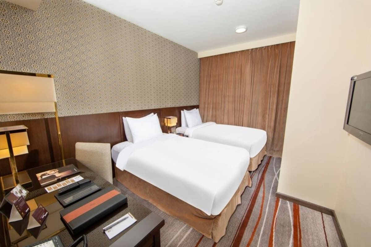 A hotel room with two beds, a desk with a lamp, and a patterned wall.
