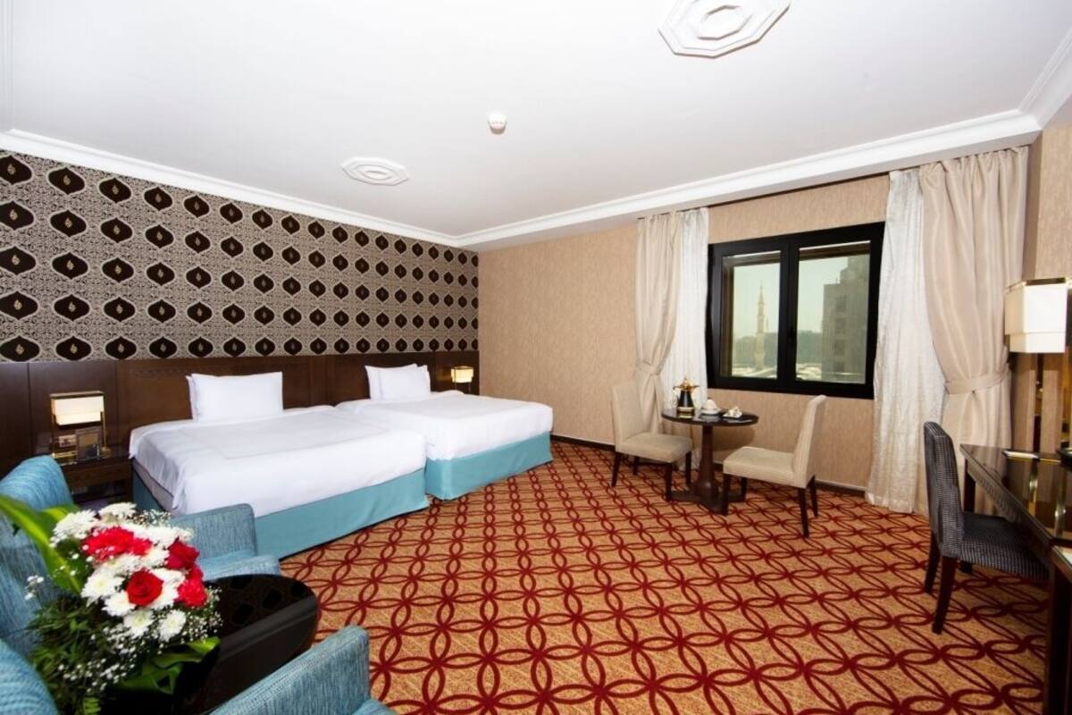A hotel room with two beds, a small table, a chair, and a decorative wall pattern.