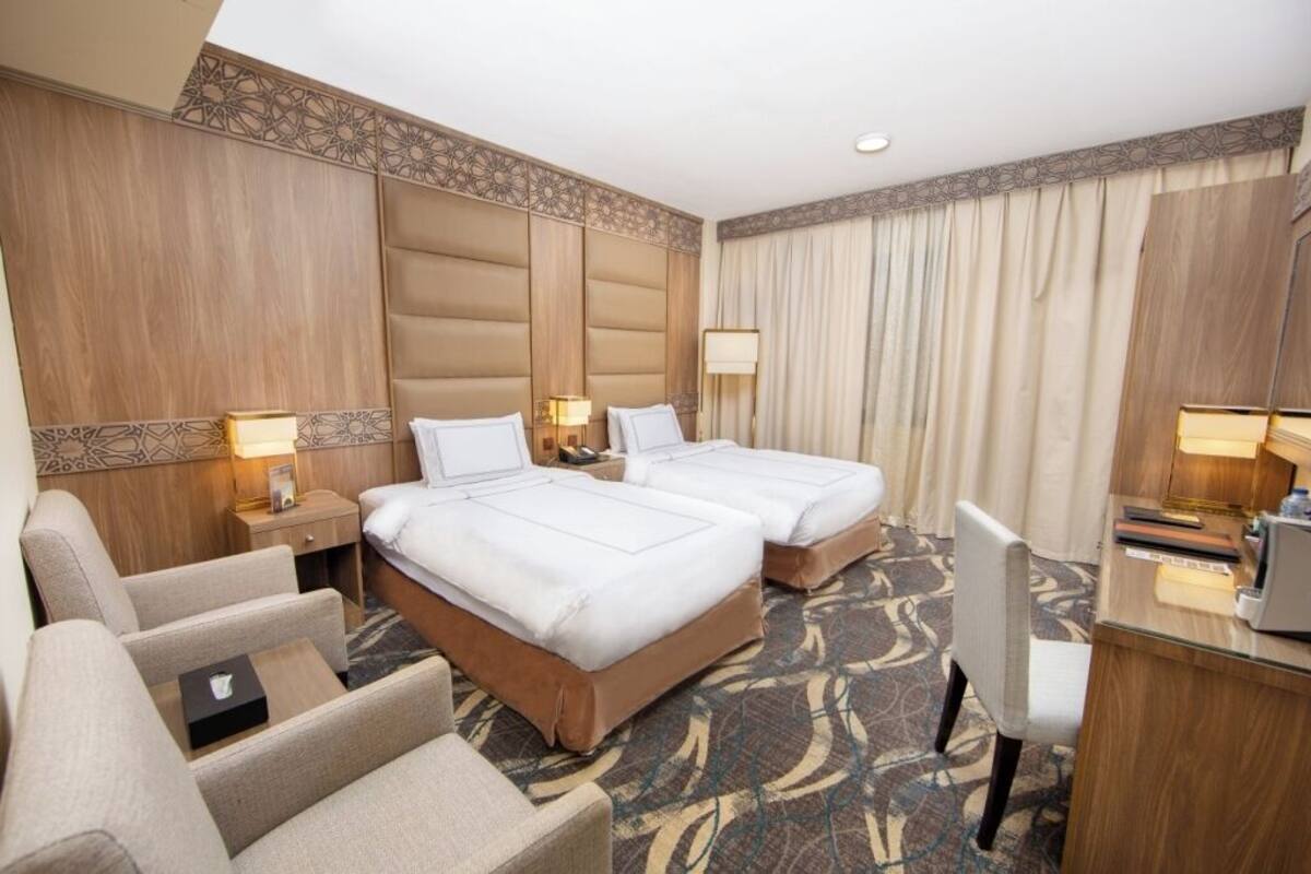 A hotel room with two beds, a desk, a chair, and a small table.