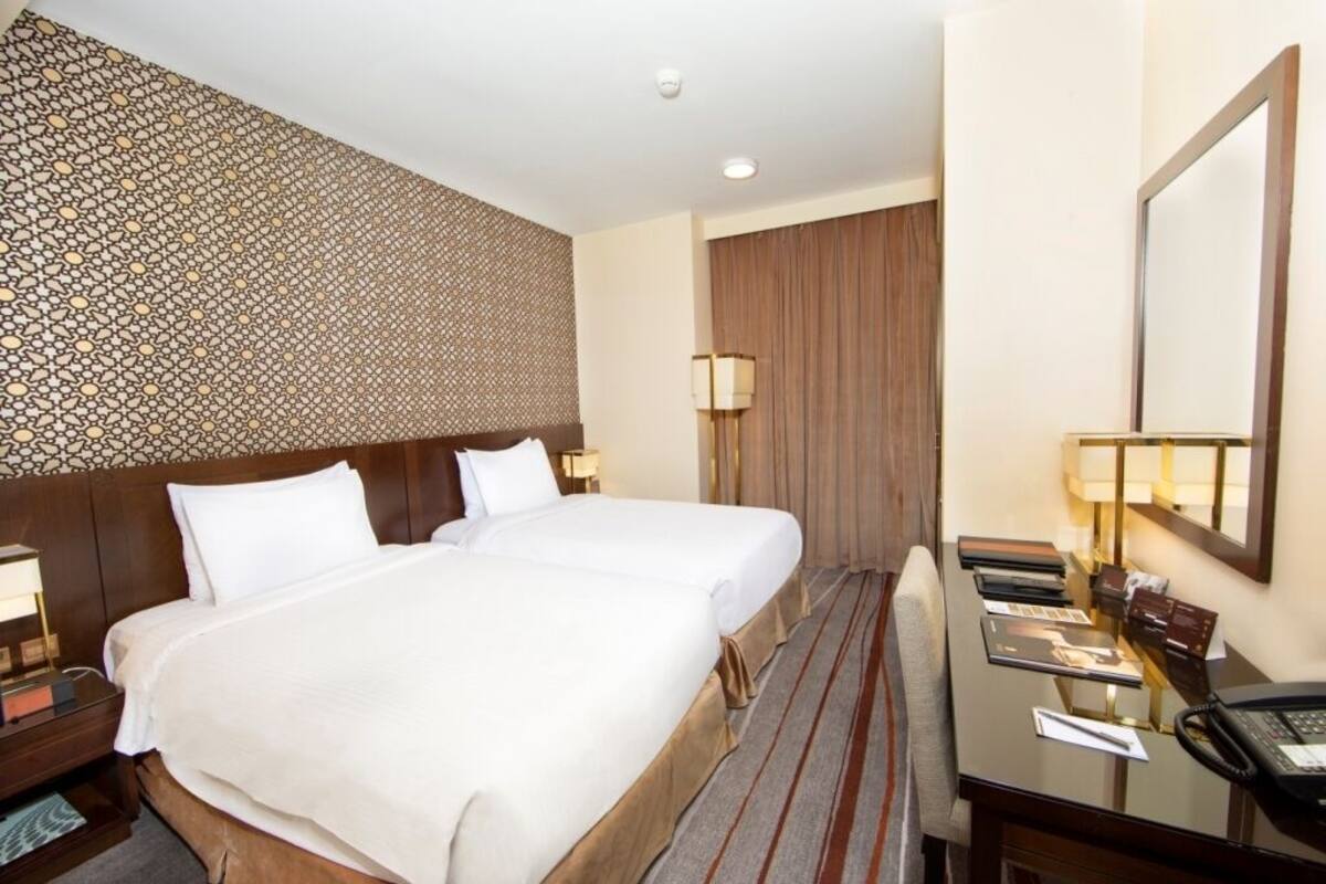 A hotel room with a large bed, a desk with a telephone, and a mirror.