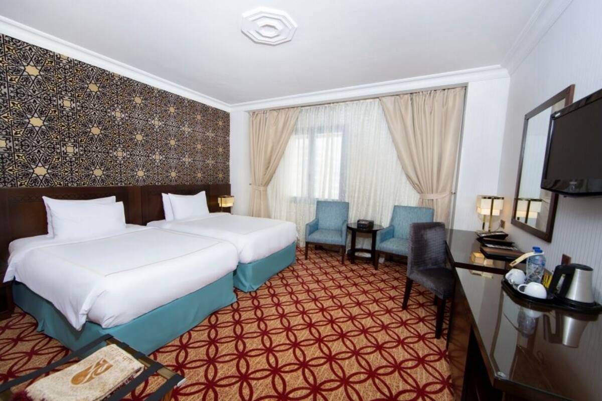 A hotel room with two beds, a desk with a chair, a TV, and a minibar.