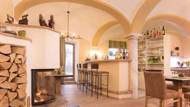 Un ambiente acogedor con chimenea, leña, una zona de bar con taburetes y una estantería con botellas.