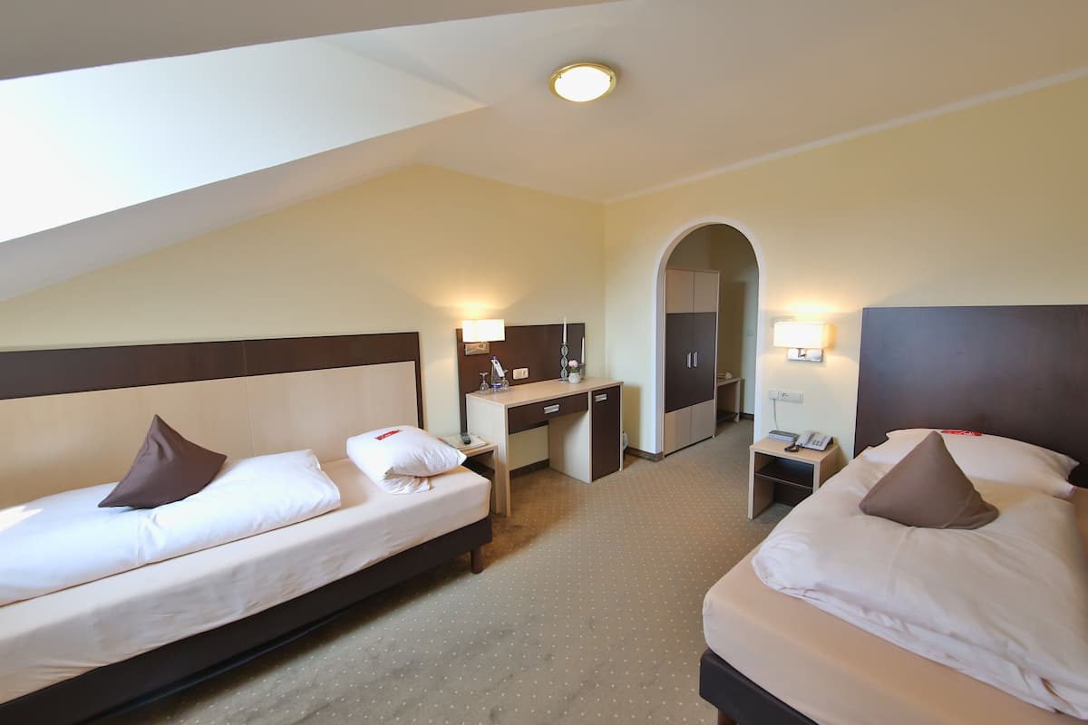 A hotel room with two beds, a desk, a chair, and a small table.
