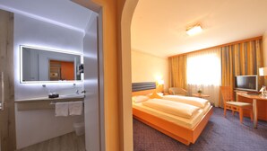 Habitación de hotel con una cama grande, un escritorio con silla, un televisor y un baño con espejo y lavabo.