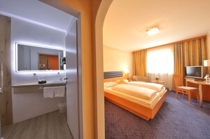 Habitación de hotel con una cama grande, un escritorio con silla, un televisor y un baño con espejo y lavabo.