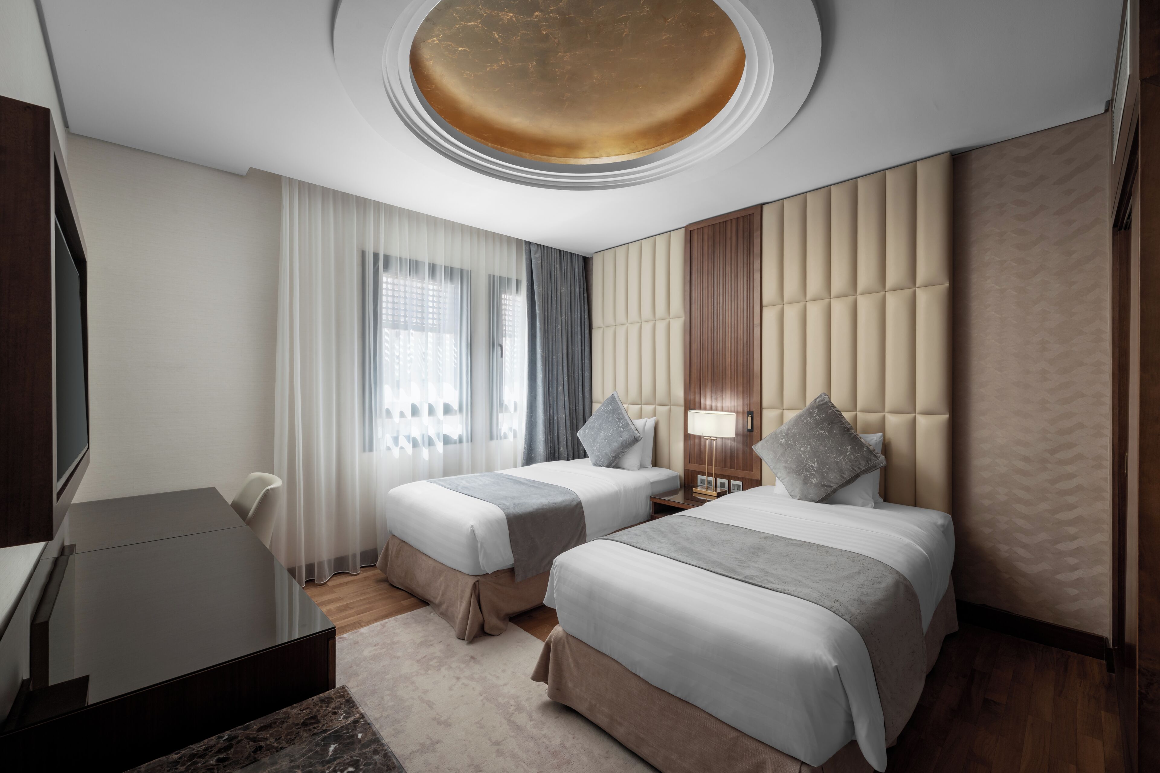 Une chambre d’hôtel avec deux lits, un bureau et une grande fenêtre avec des rideaux.
