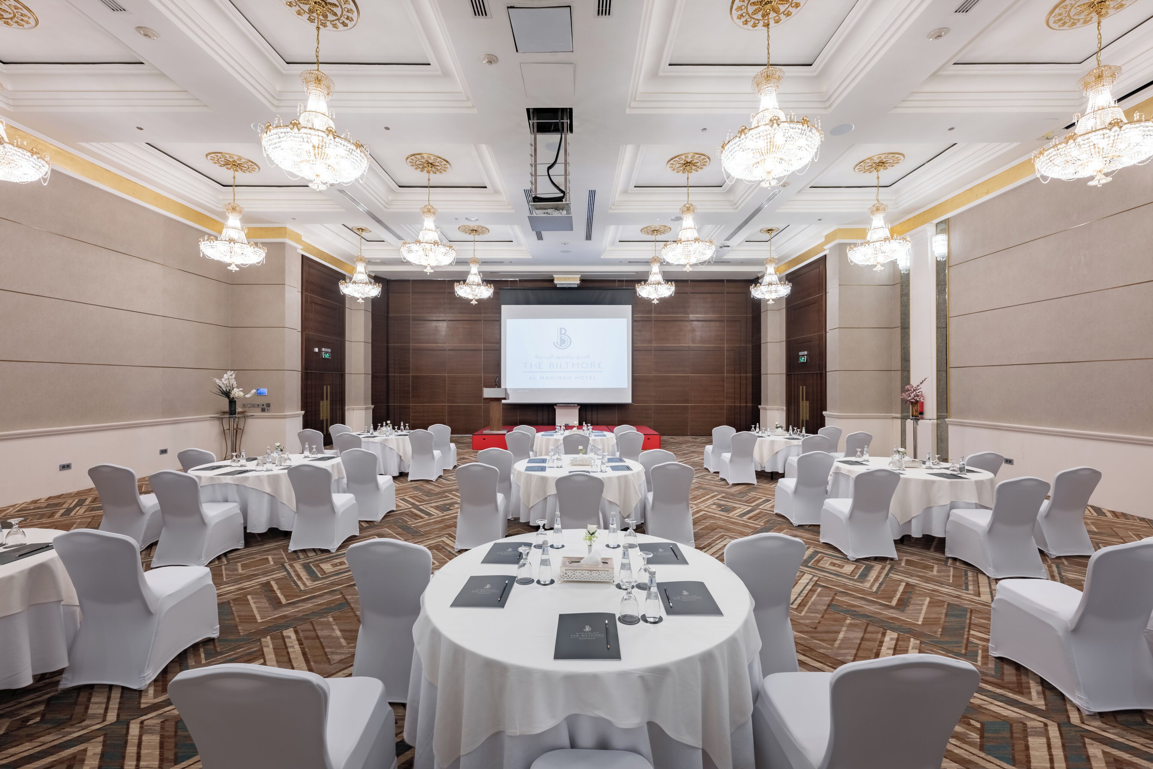 A conference room with round tables, white chairs, and chandeliers.