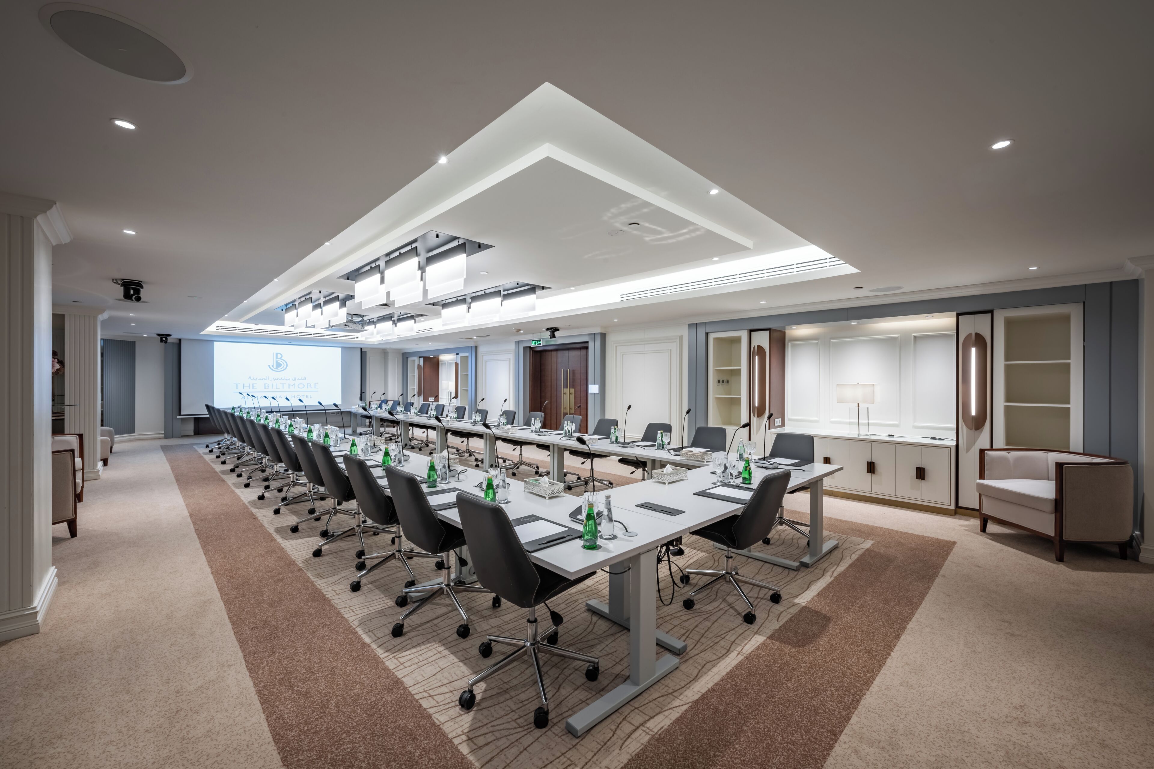 A conference room with a long table, chairs, and a projector screen.