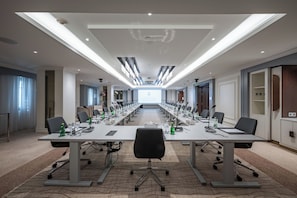 A conference room with a long table, chairs, microphones, and a projection screen. - The Biltmore Almadinah Hotel (Madinah)