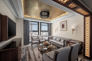 A modern living room with a large flat-screen TV, comfortable seating, a coffee table, and a view of a cityscape through large windows.