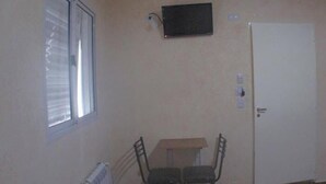 Una habitación pequeña con una ventana, una puerta, un radiador y una mesa pequeña con dos sillas.