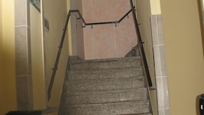Una escalera con barandilla, paredes color beige y piso de baldosas.