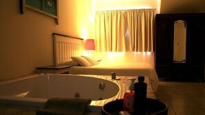 Et hotelværelse med et stort badekar, en seng, et natbord og et spejl.