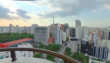 Paisagem urbana com arranha-céus, uma torre imponente e uma área verde em primeiro plano.