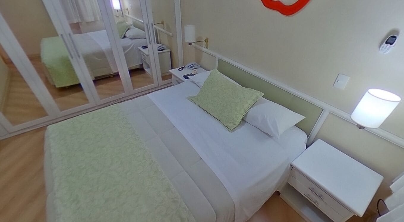 A hotel room with a bed, a nightstand, a lamp, and a mirror.