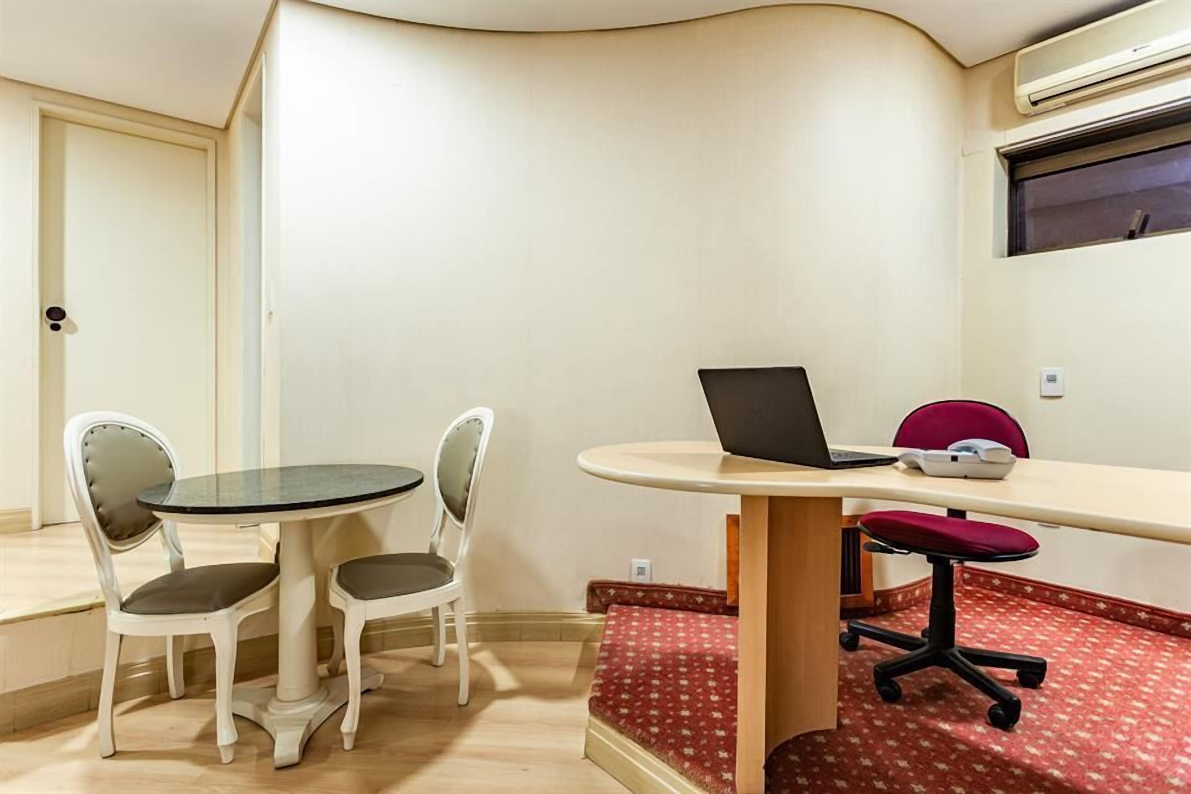 A room with a round table, two white chairs, a laptop, and a red office chair.