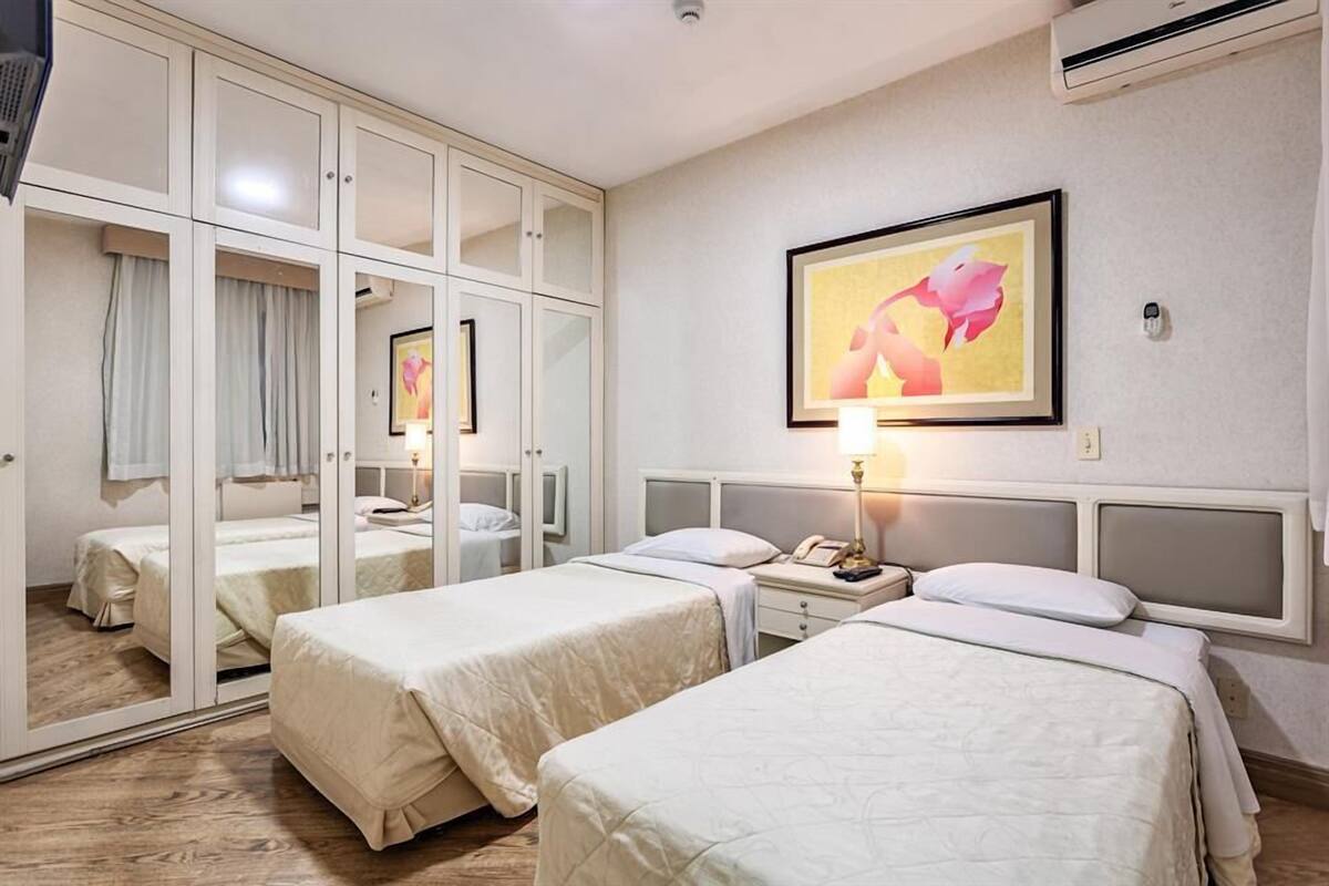 Habitación de hotel con dos camas, un espejo grande, un cuadro en la pared y una mesita de noche con lámpara.