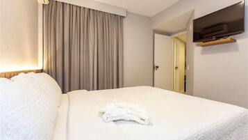 Una habitación de hotel con una cama bien hecha, un televisor de pantalla plana montado en la pared y una puerta que da a otra habitación.