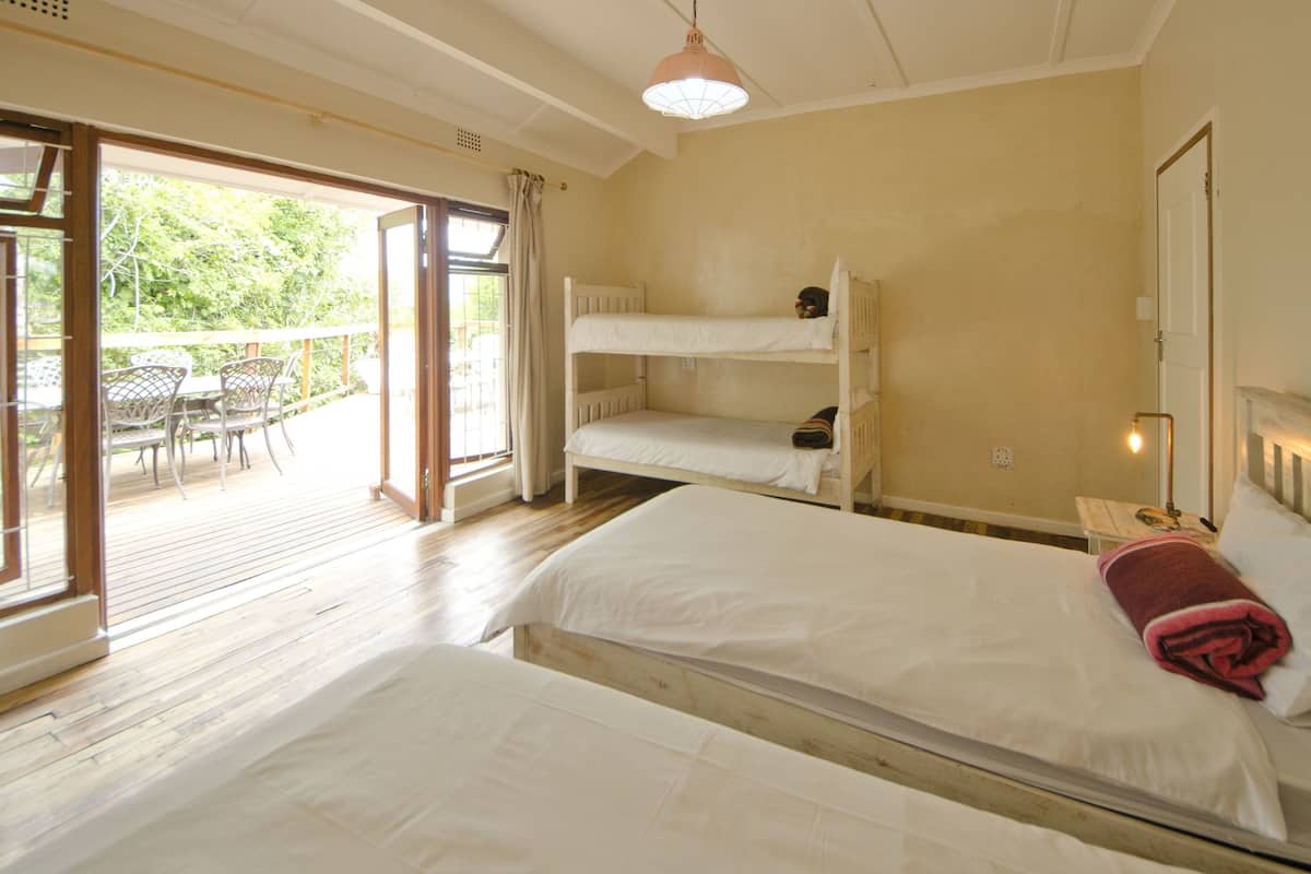 Une chambre avec un grand lit, un lit plus petit et un lit superposé. Une porte-fenêtre coulissante donne accès à un patio extérieur équipé d’une table et de chaises.
