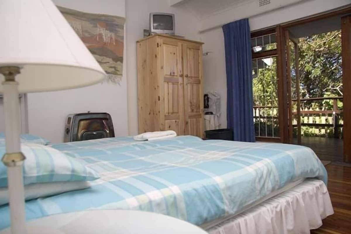 Une chambre à coucher avec un lit, une armoire en bois, un téléviseur posé sur le dessus, et une vue sur l’extérieur grâce à une porte vitrée.