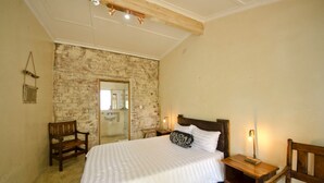 A bedroom with a brick wall, a wooden bed frame, a bedside table, and a chair. - Island Vibe Knysna Hostel (Knysna)