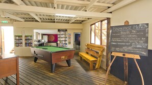 A billiards table in a room with a chalkboard displaying breakfast menu options. - Island Vibe Knysna Hostel (Knysna)