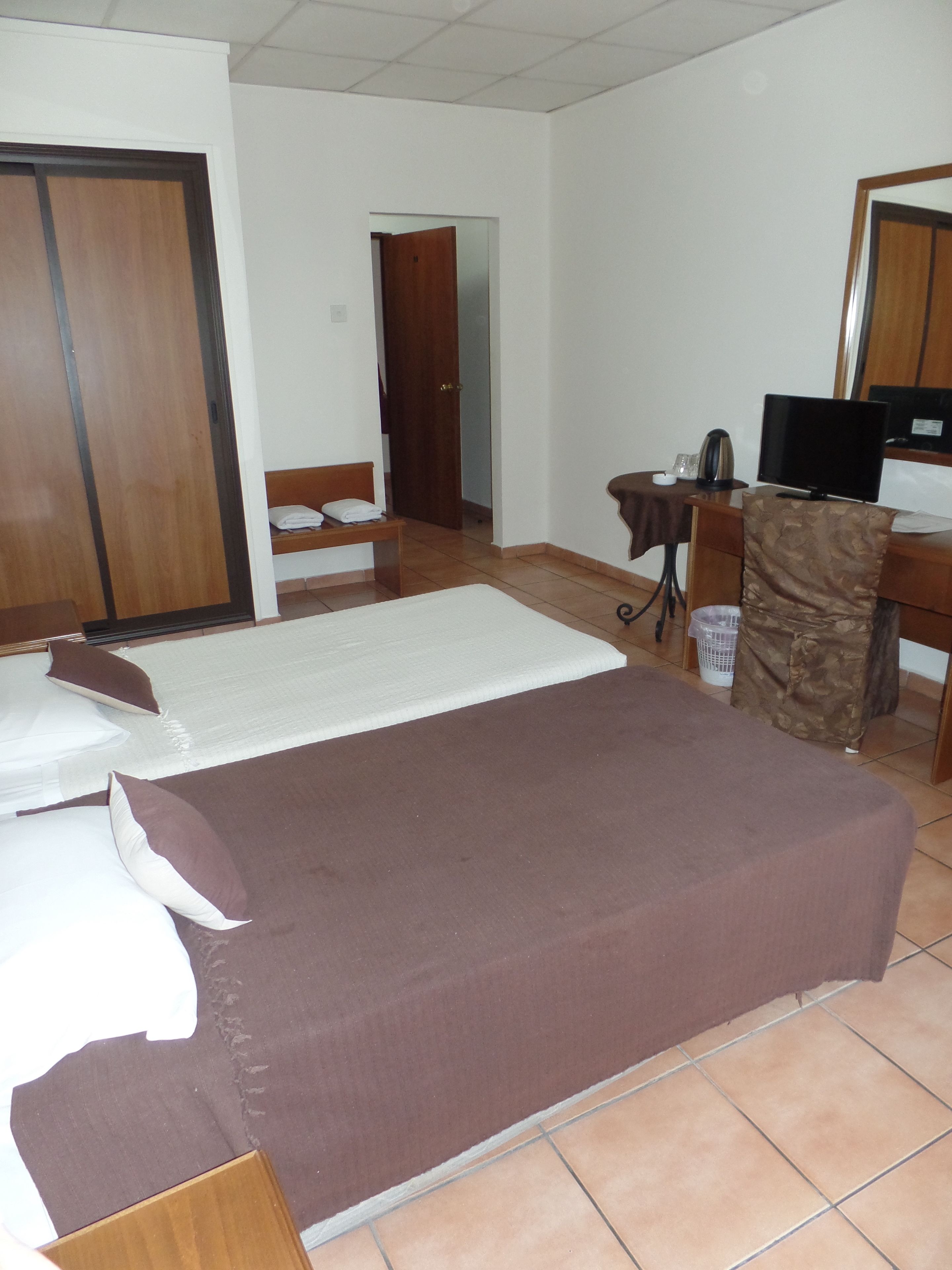 A hotel room with a bed, a desk, a chair, a television, and a wardrobe.