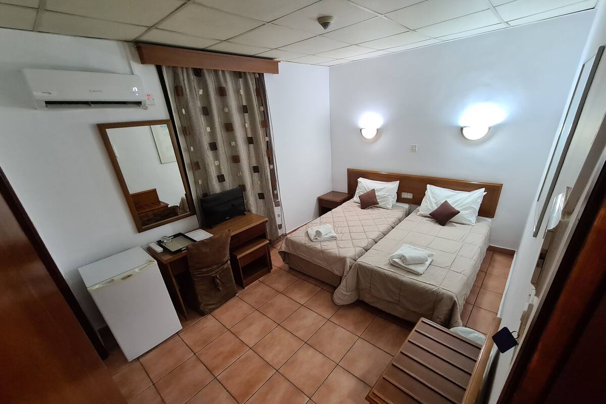 A hotel room with two beds, a desk, a chair, a television, and a mirror.