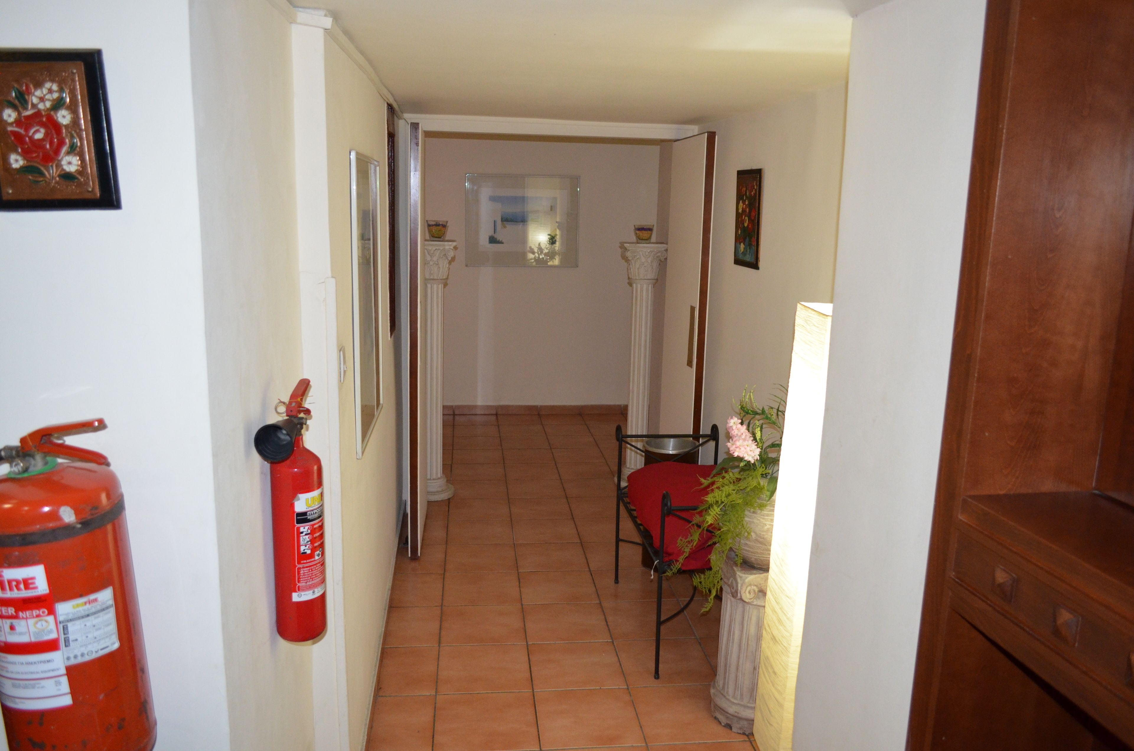 A hallway with a fire extinguisher, a chair, and a potted plant.