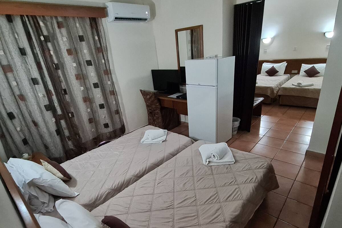 A hotel room with two beds, a desk, a refrigerator, and a TV.