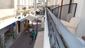 A narrow street with buildings on either side, a pedestrian walkway, and a balcony with a metal railing.