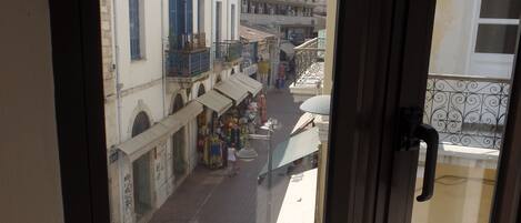 A view from a window overlooking a street with buildings, shops, and a pedestrian.