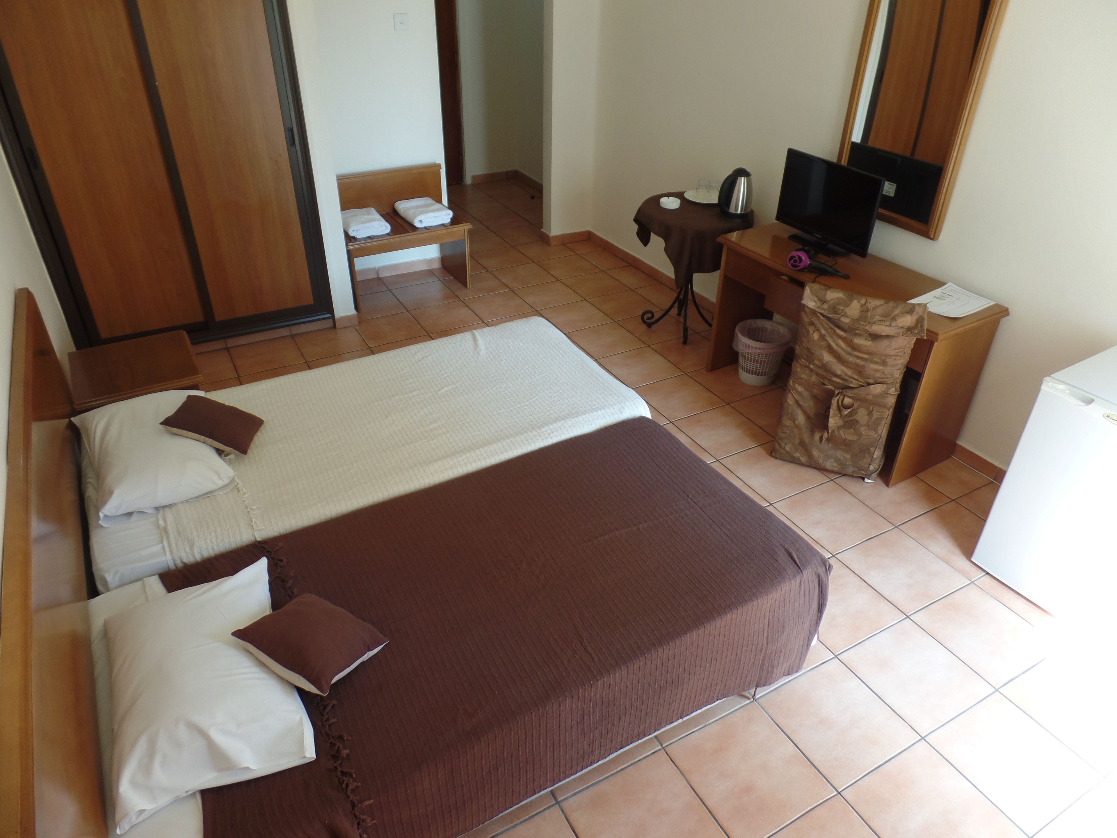 A hotel room with a large bed, a desk with a computer and a television, a small table with a kettle, and a wardrobe.