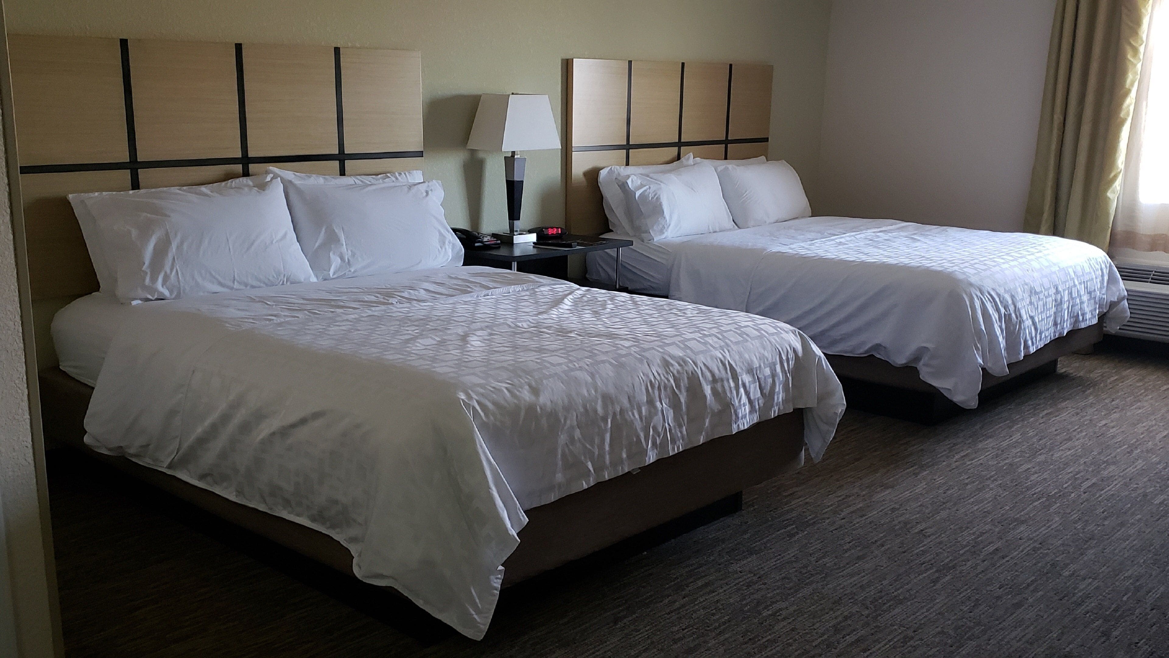 A hotel room with two beds, a nightstand, a lamp, and a digital clock.