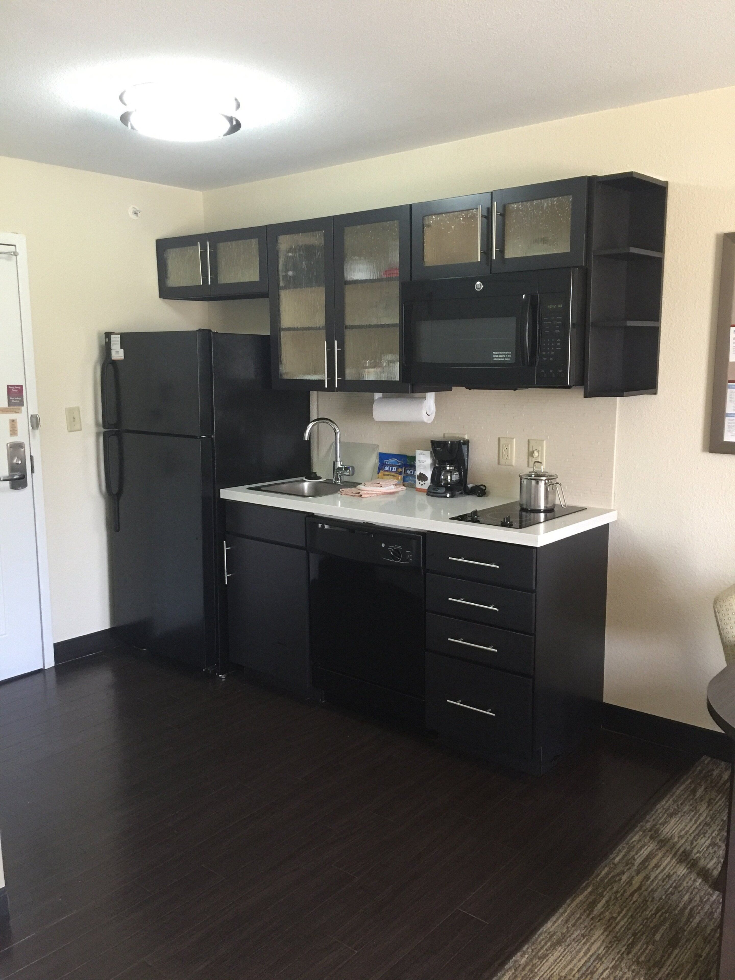 A compact kitchen with black cabinets, a refrigerator, a microwave, and a coffee maker.