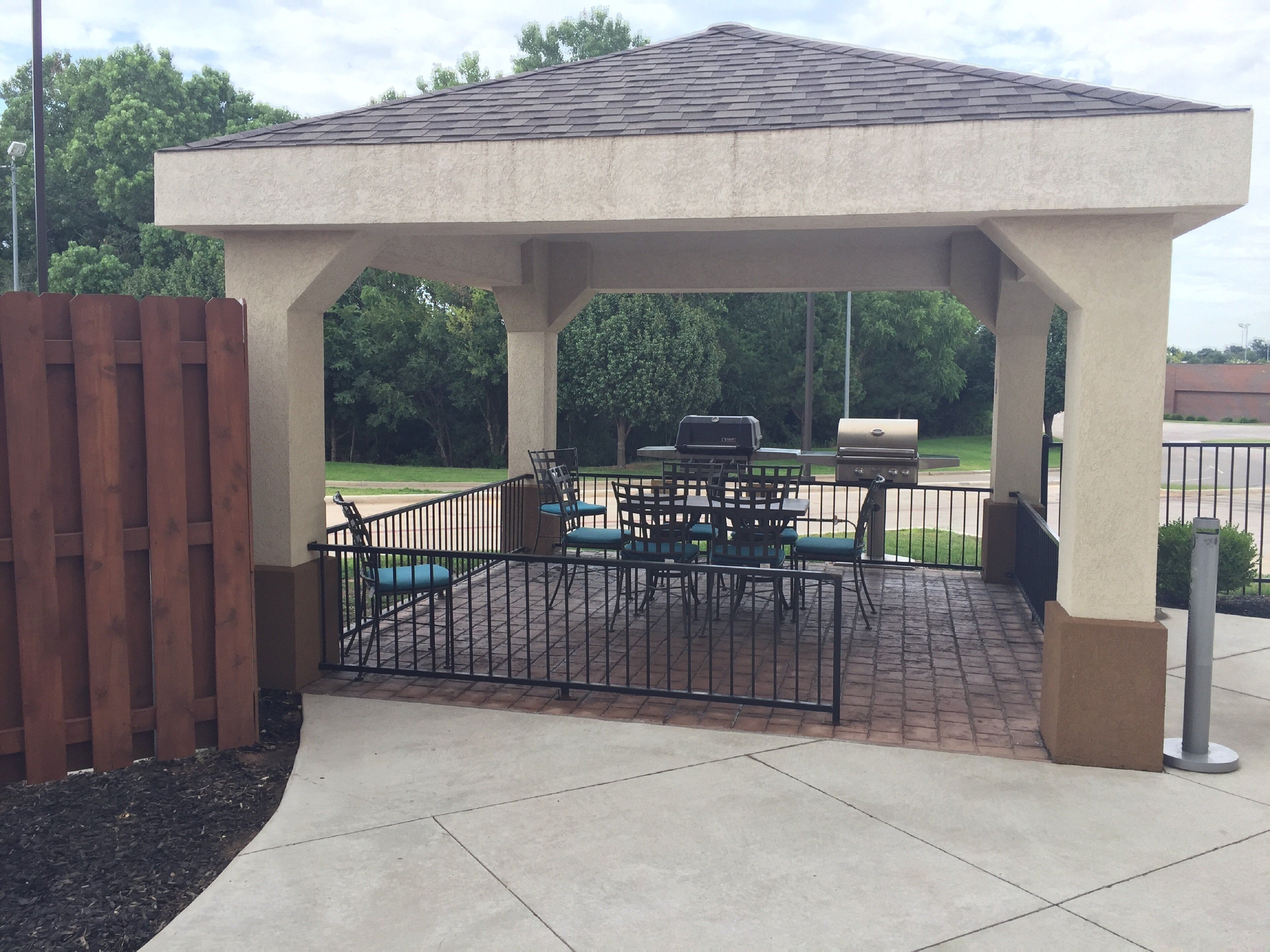 A covered patio area with a grill, seating, and a gated entrance.