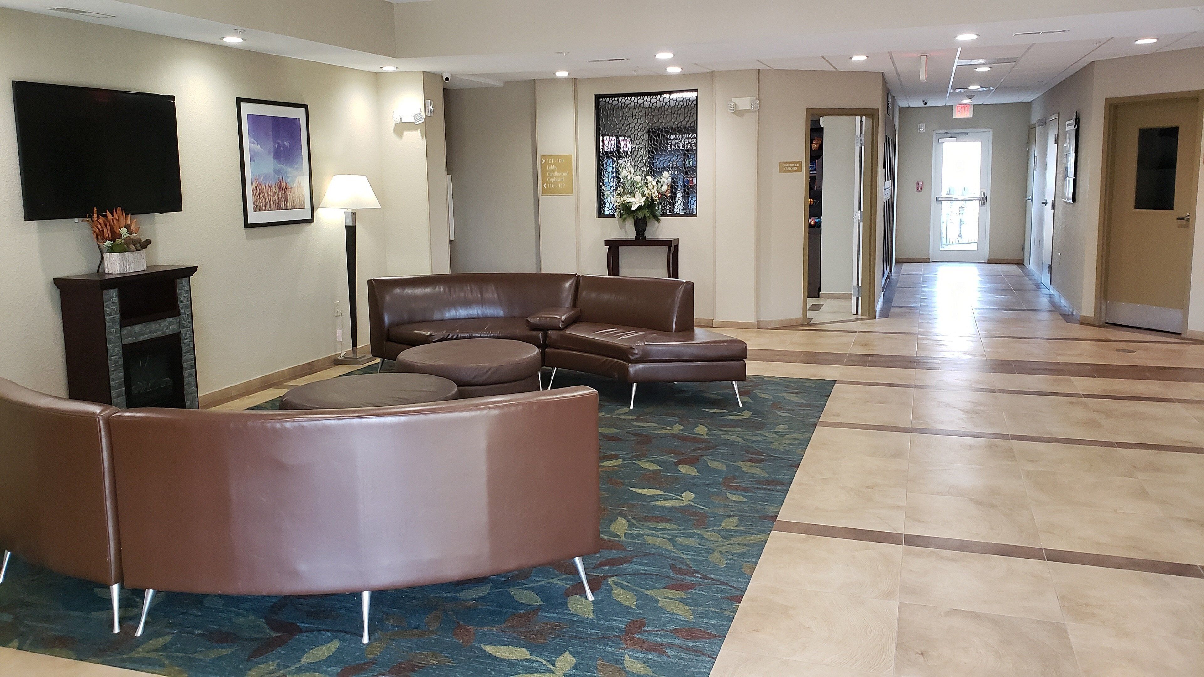 A hotel lobby with a seating area, a flat-screen TV, a framed picture, and a carpeted floor.