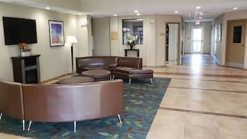 A hotel lobby with a seating area, a flat-screen TV, a framed picture, and a carpeted floor.