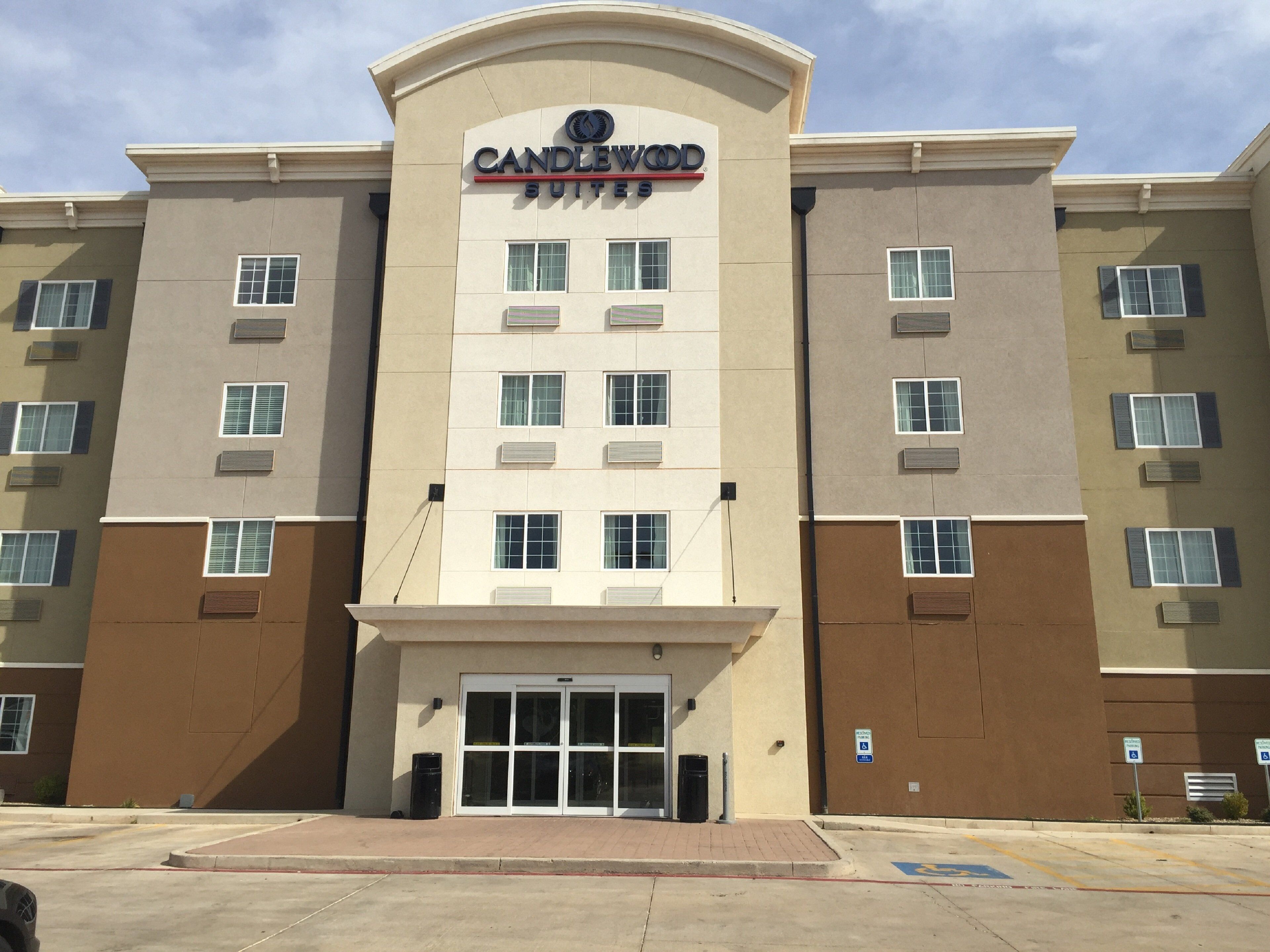 A multi-story hotel with a central entrance, air conditioning units on each floor, and a parking lot with handicapped parking signs.