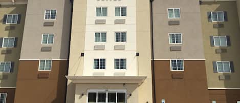 A multi-story hotel with a central entrance, air conditioning units on each floor, and a parking lot with handicapped parking signs.