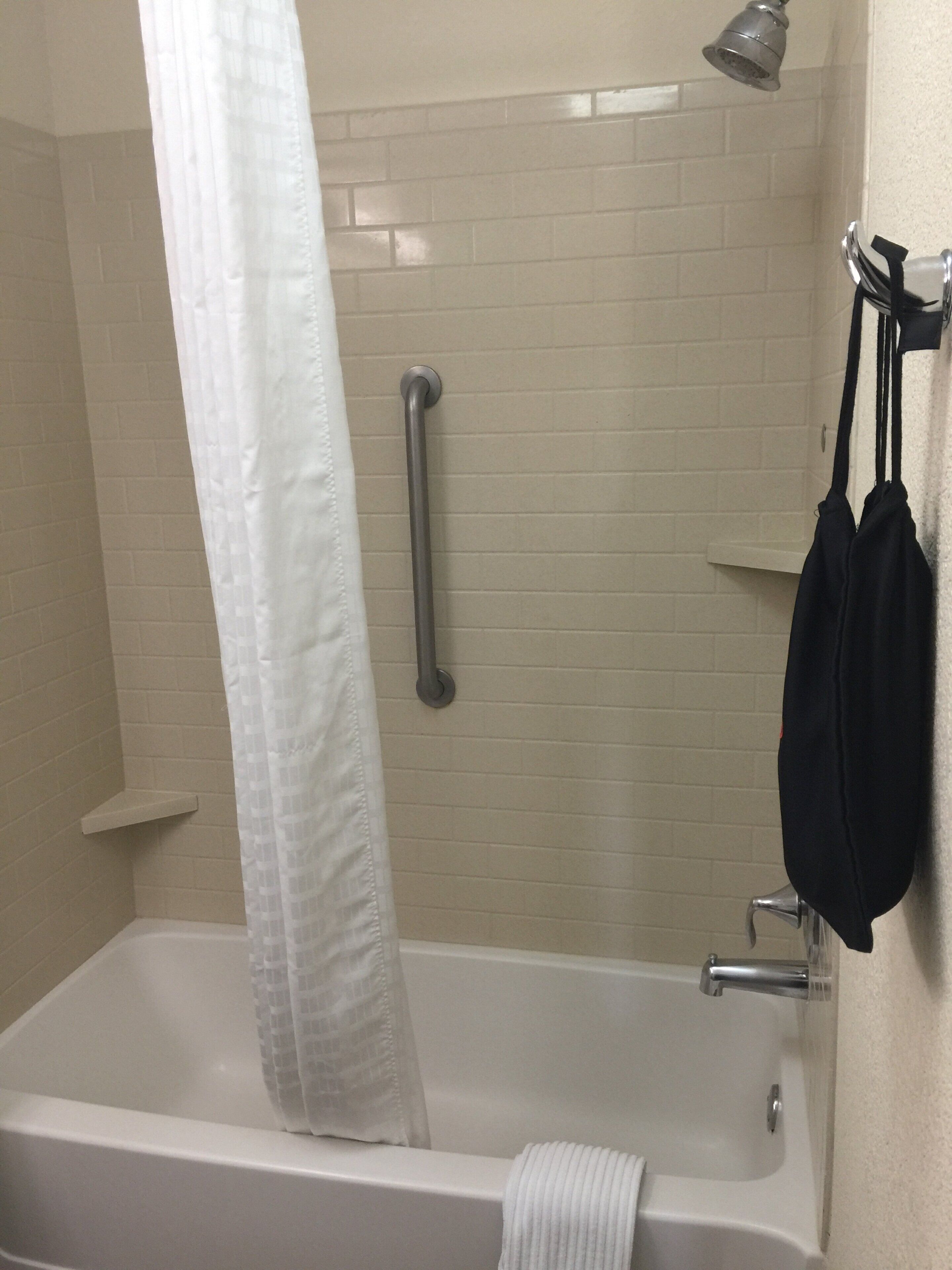 A bathroom with a bathtub, a shower, and a handrail.