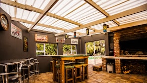 A covered outdoor seating area with a brick fireplace, wooden tables and chairs, and various signs on the walls. - The Russel Guesthouse (Gqeberha (Port Elizabeth))