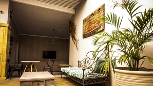 A cozy living room with a sofa, a coffee table, a TV, and a large potted plant. - The Russel Guesthouse (Gqeberha (Port Elizabeth))