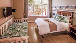 A bedroom with a bed, a small seating area, a TV, and a window with curtains. - The Russel Guesthouse (Gqeberha (Port Elizabeth))