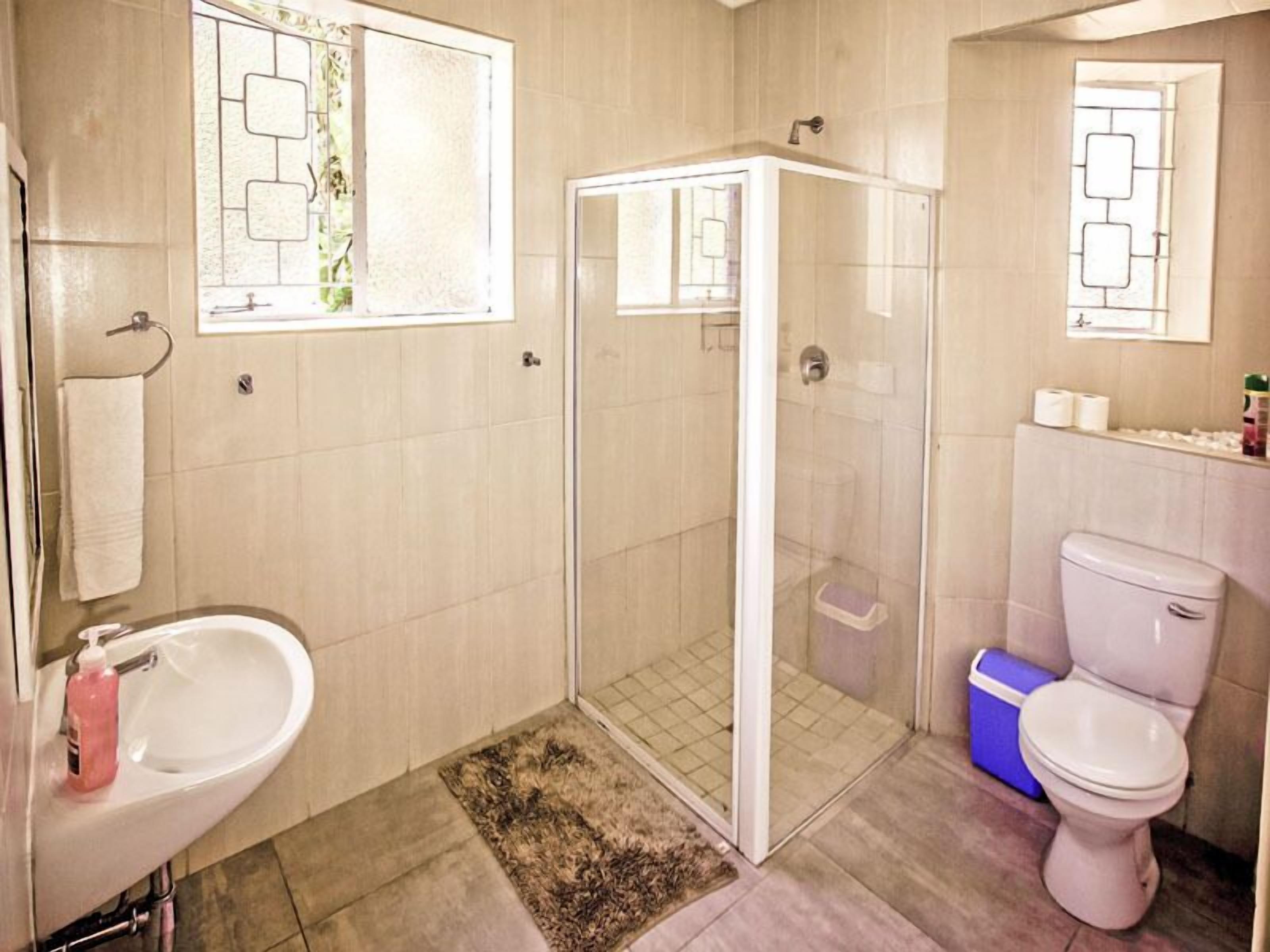A bathroom with a shower, toilet, sink, and a window with a geometric design.