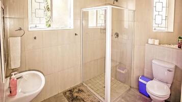 A bathroom with a shower, toilet, sink, and a window with a geometric design.